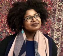 Picture of Dr. Andrea S Bryant with blue earrings, an afro and a pink and blue scarf. Wearing glasses and smiling, looking upwards at an angle.  