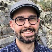 A bearded man with glasses wearing a grey hat